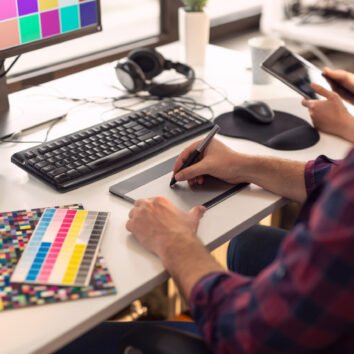 Designer working on a new project in an office; web designer drawing on a drawing pad and choosing colors from a color palette. Focus on the tip of the pen and the fingers